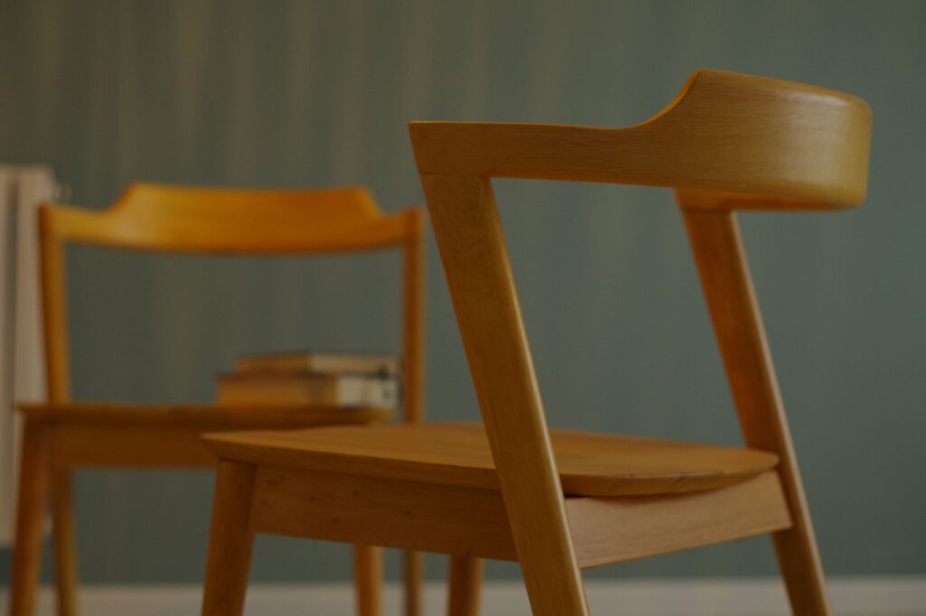 Two plain wooden chairs drawn up to a table, photographed softly against a muted green wall